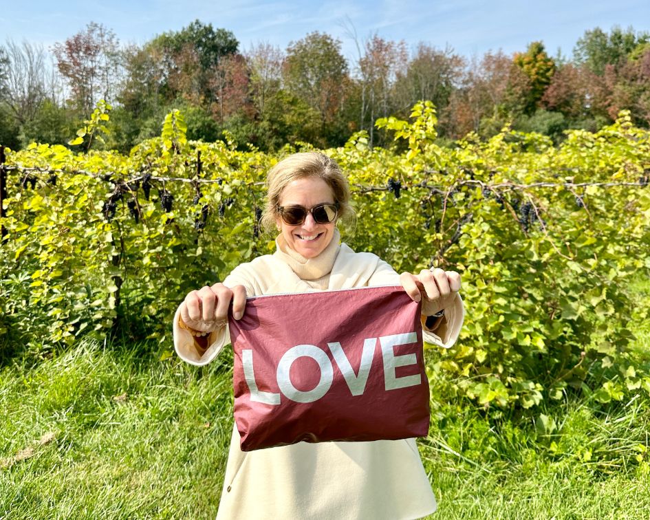 Woman standing in winery holding cabernet zipper pouch with "LOVE"