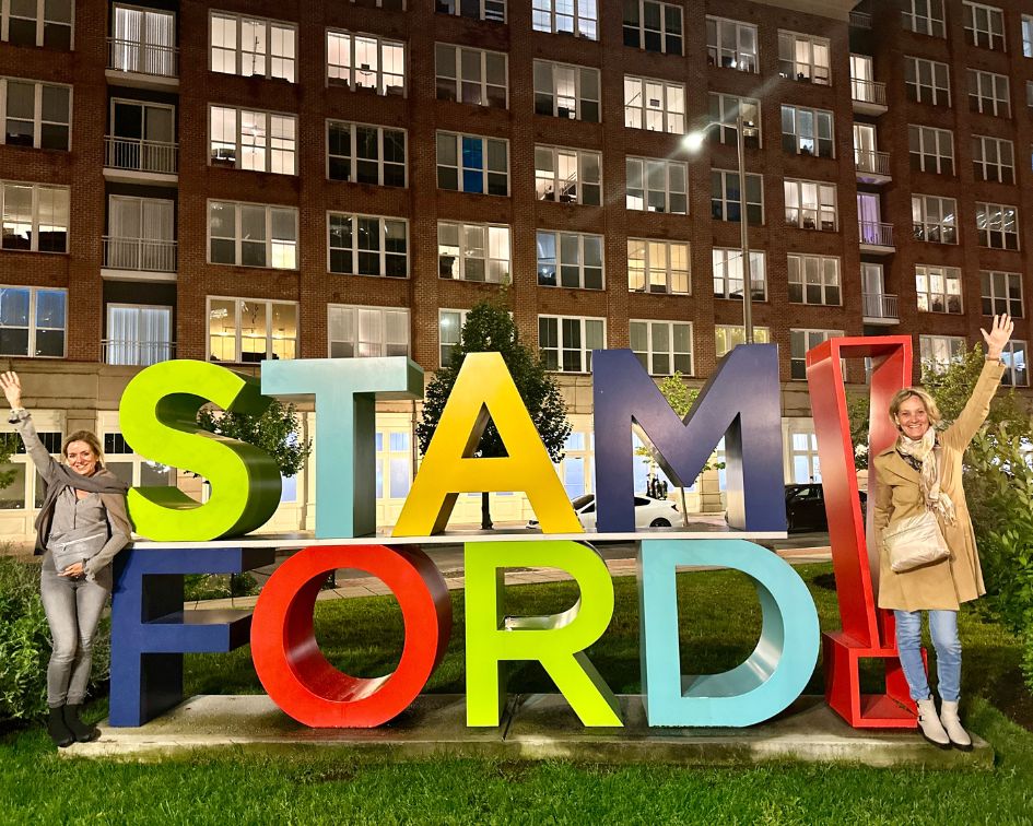 Two women outdoors standing in front of Stamford! Both women wearing crossbody Puffer Purse bags.