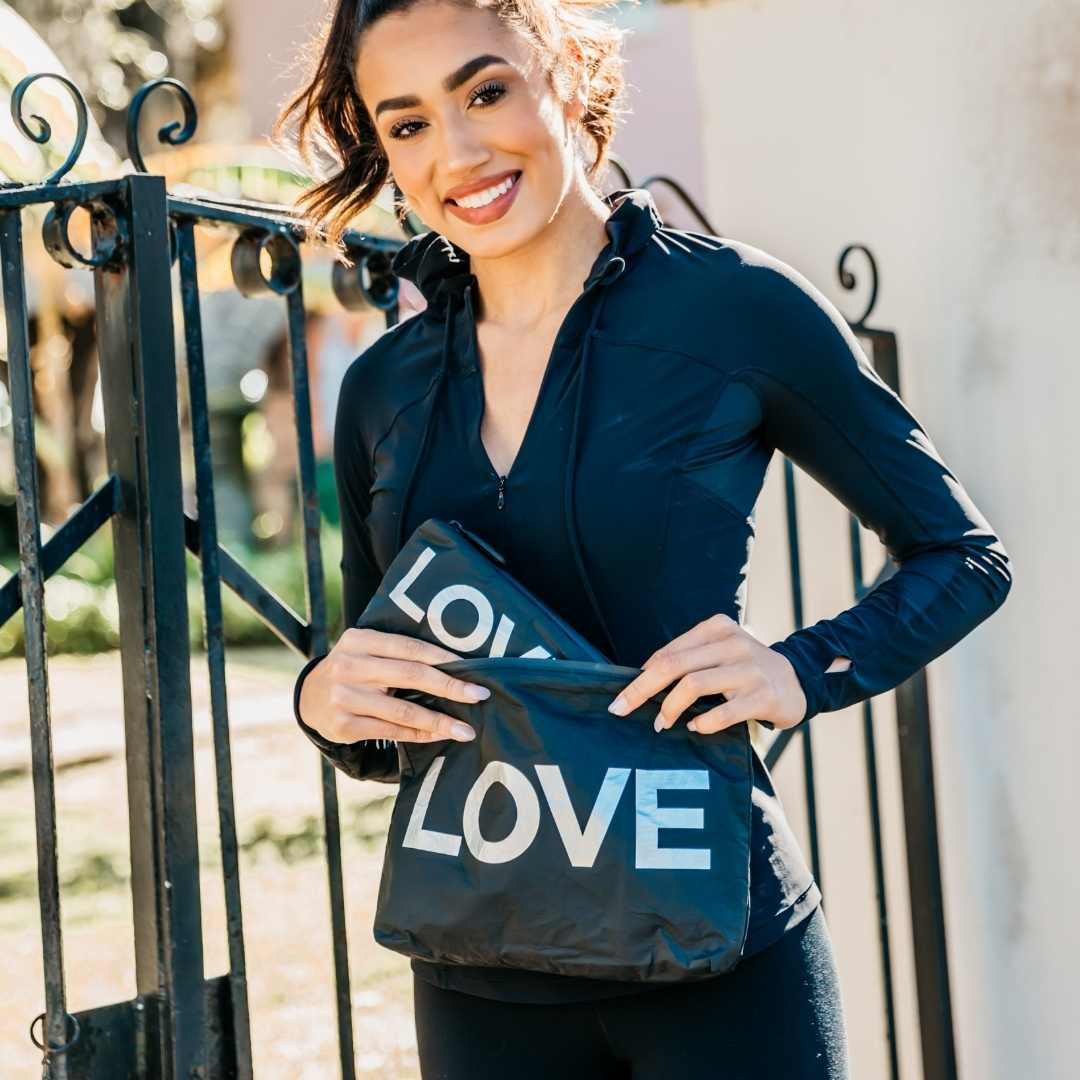 Woman holding a black bag with 'LOVE' printed on it, standing outdoors.