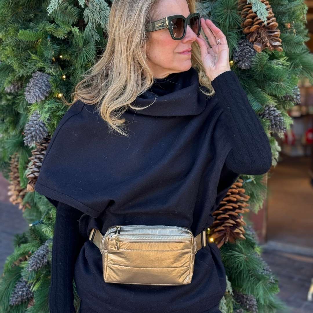 Women in a black sweater wearing a gold crossbody belt bag.