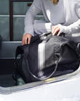 Black weekender bag with silver and pewter center stripes packed inside an airplane doorway.