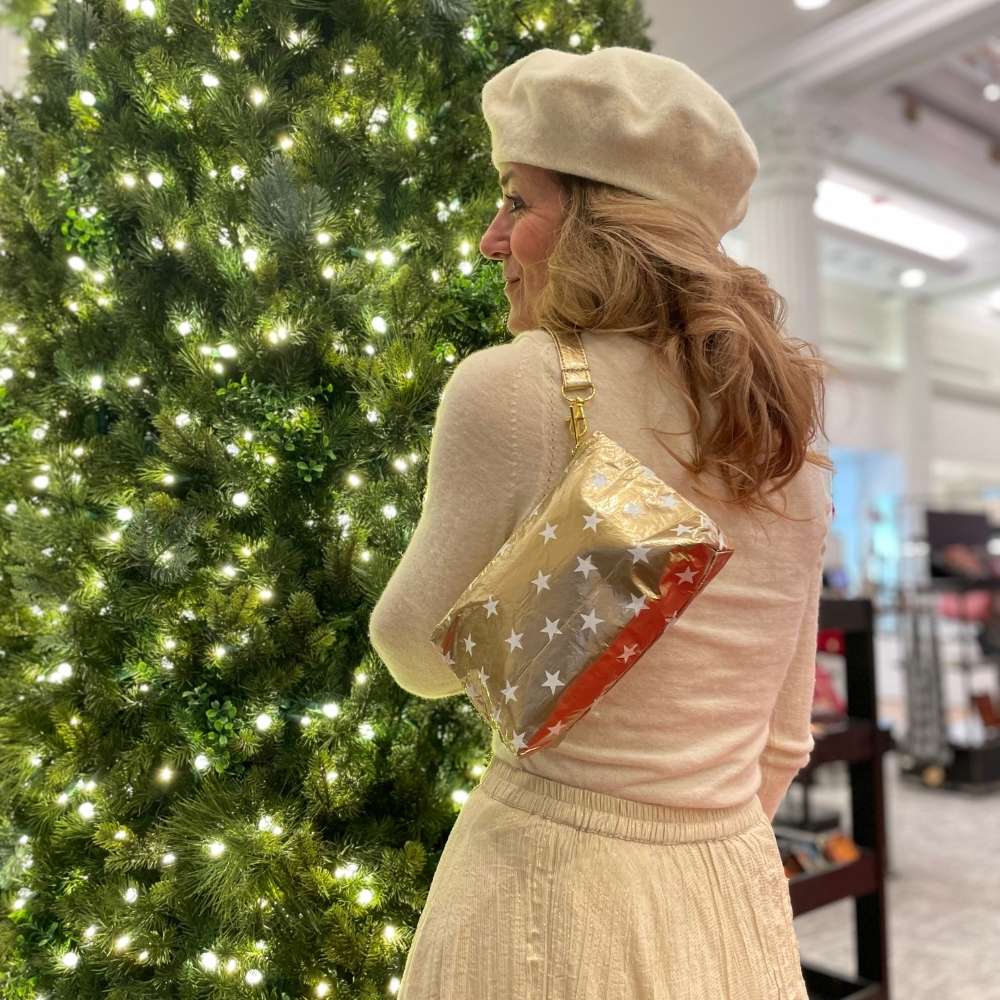 Woman wearing gold wristlet with stars dressed in cream sweater, skirt and beret