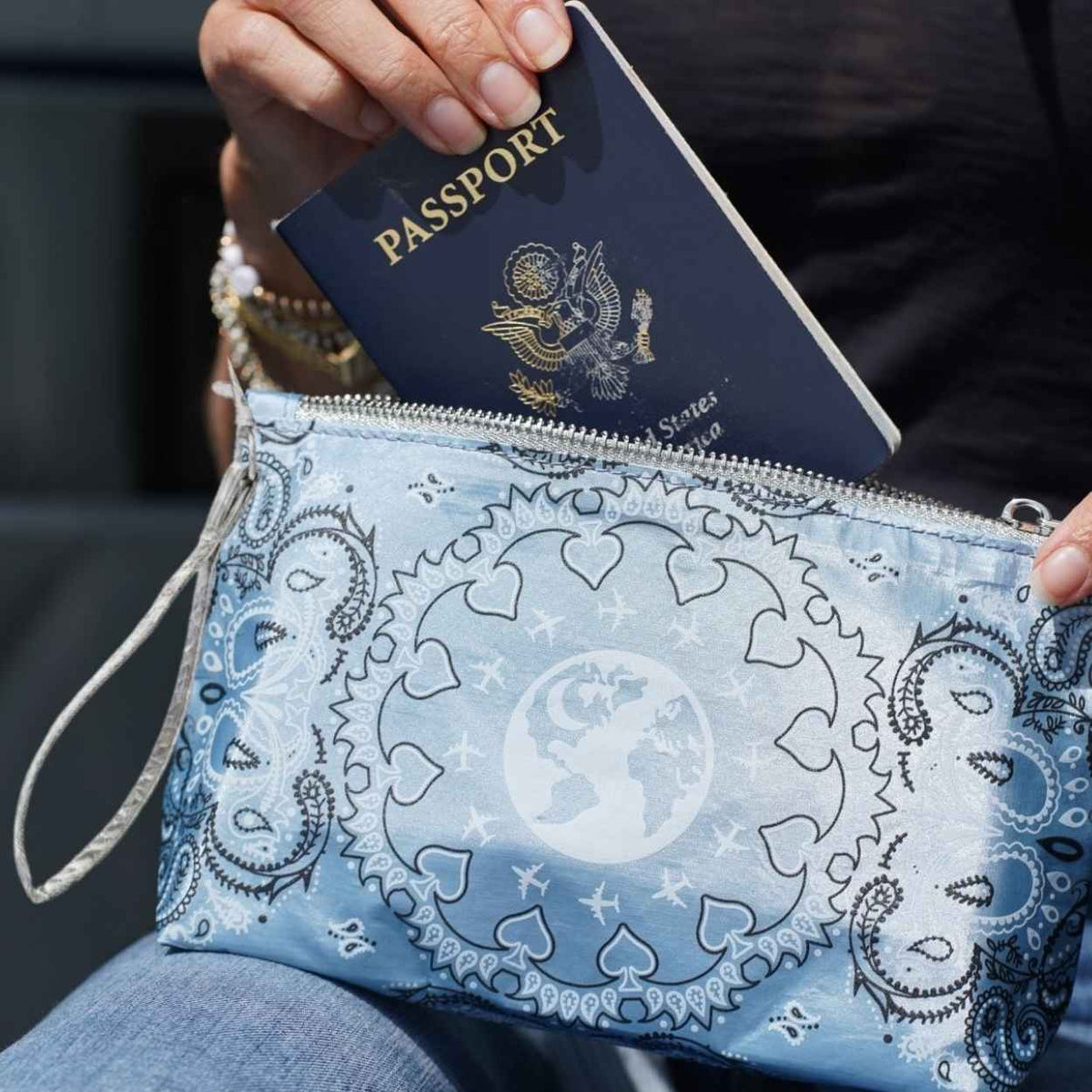 Close up of hand putting passport into blue travel pouch wristlet with bandana print against dark background