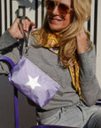 Woman holding a purple bag with a star design, wearing sunglasses and a patterned scarf.