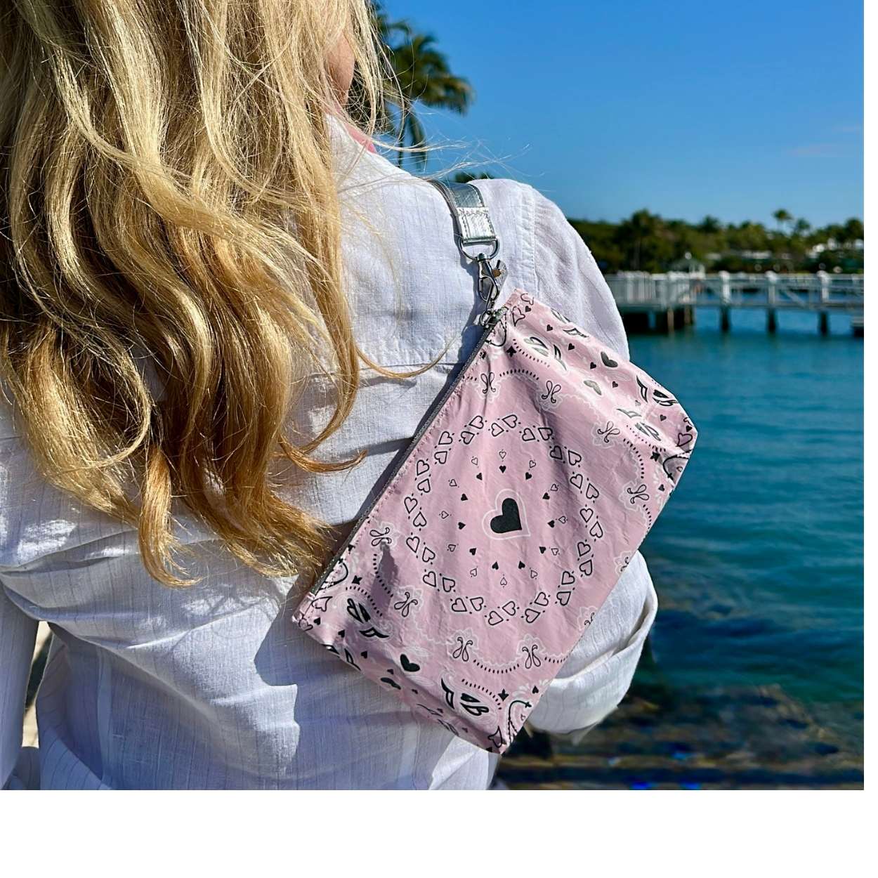 Person holding a pink bandana print bag with black hearts by a waterfront