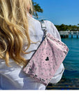 Person holding a pink bandana print bag with black hearts by a waterfront