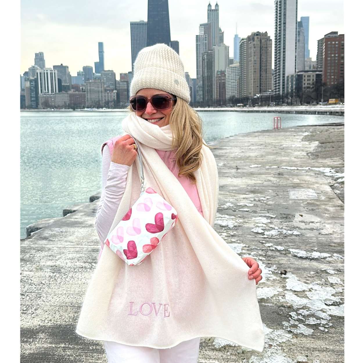 Woman carrying wristlet with pink heart print in winter with city view behind her.