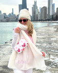 Woman carrying wristlet with pink heart print in winter with city view behind her.