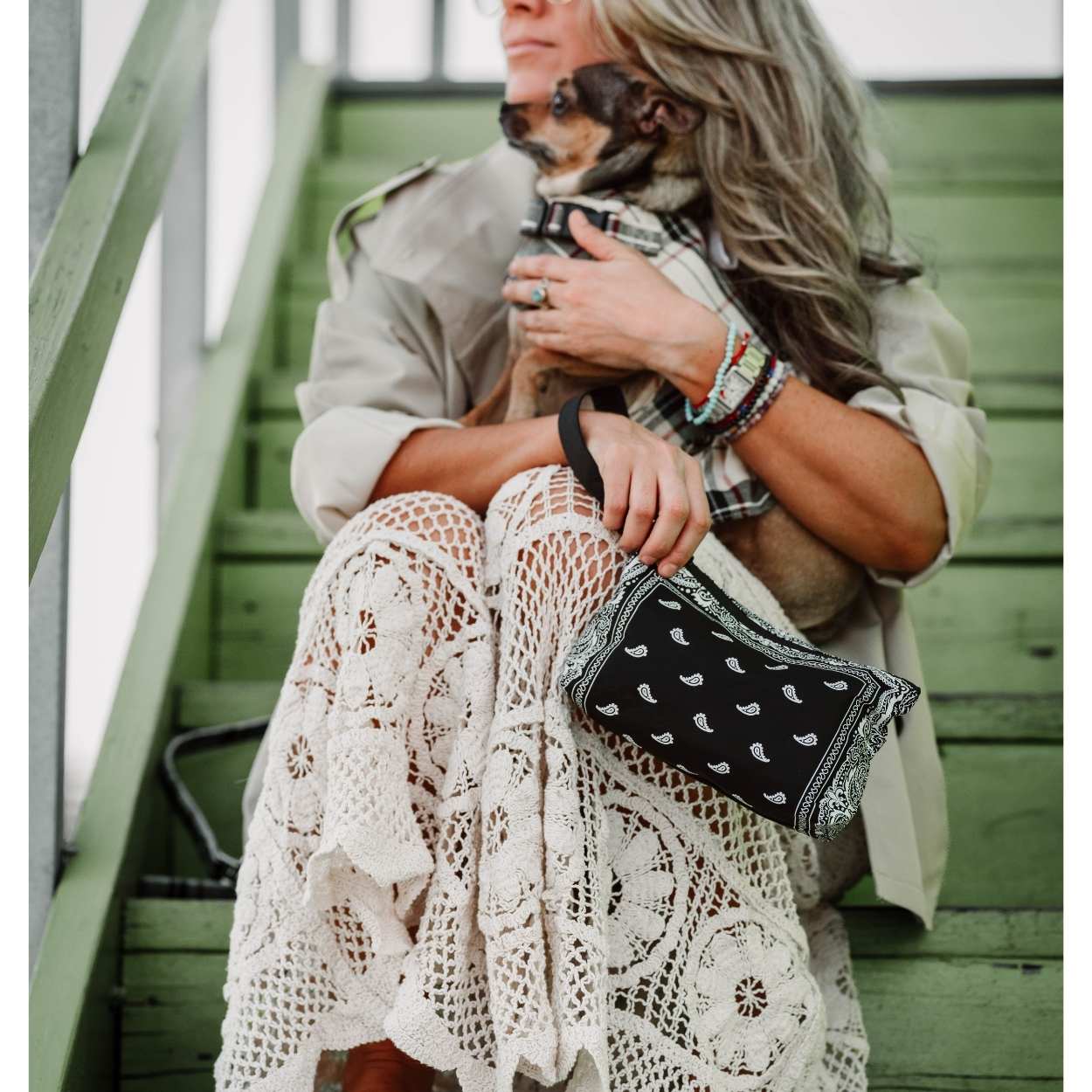 Woman carrying black bandana print wristlet with dog on green stairs