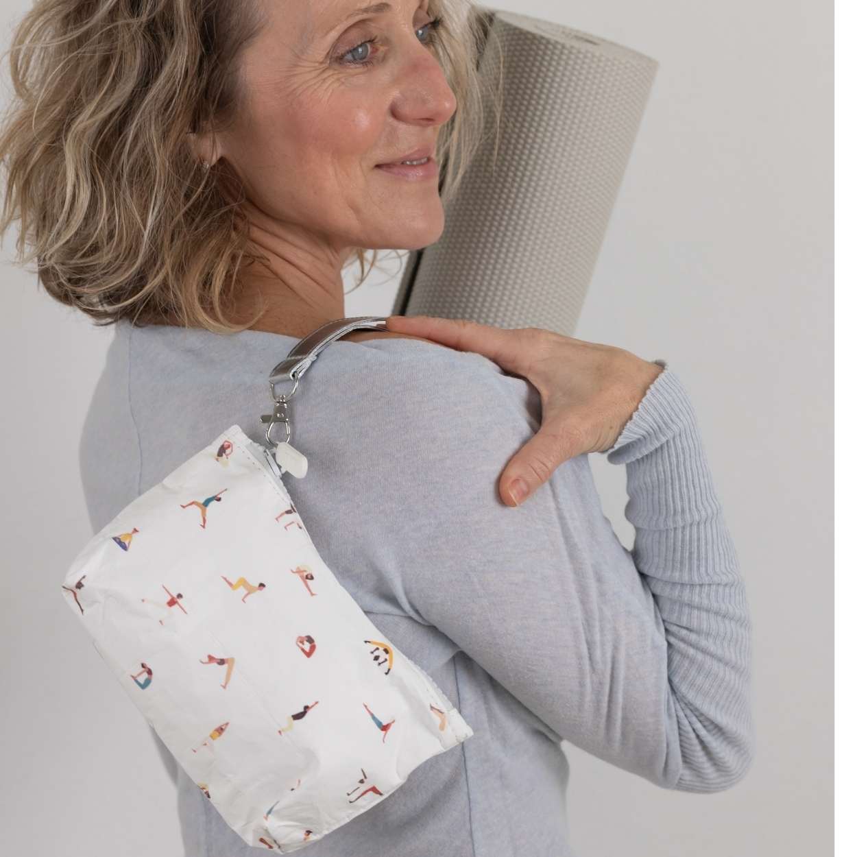 Woman holding a white pouch with colorful yoga poses on a plain background