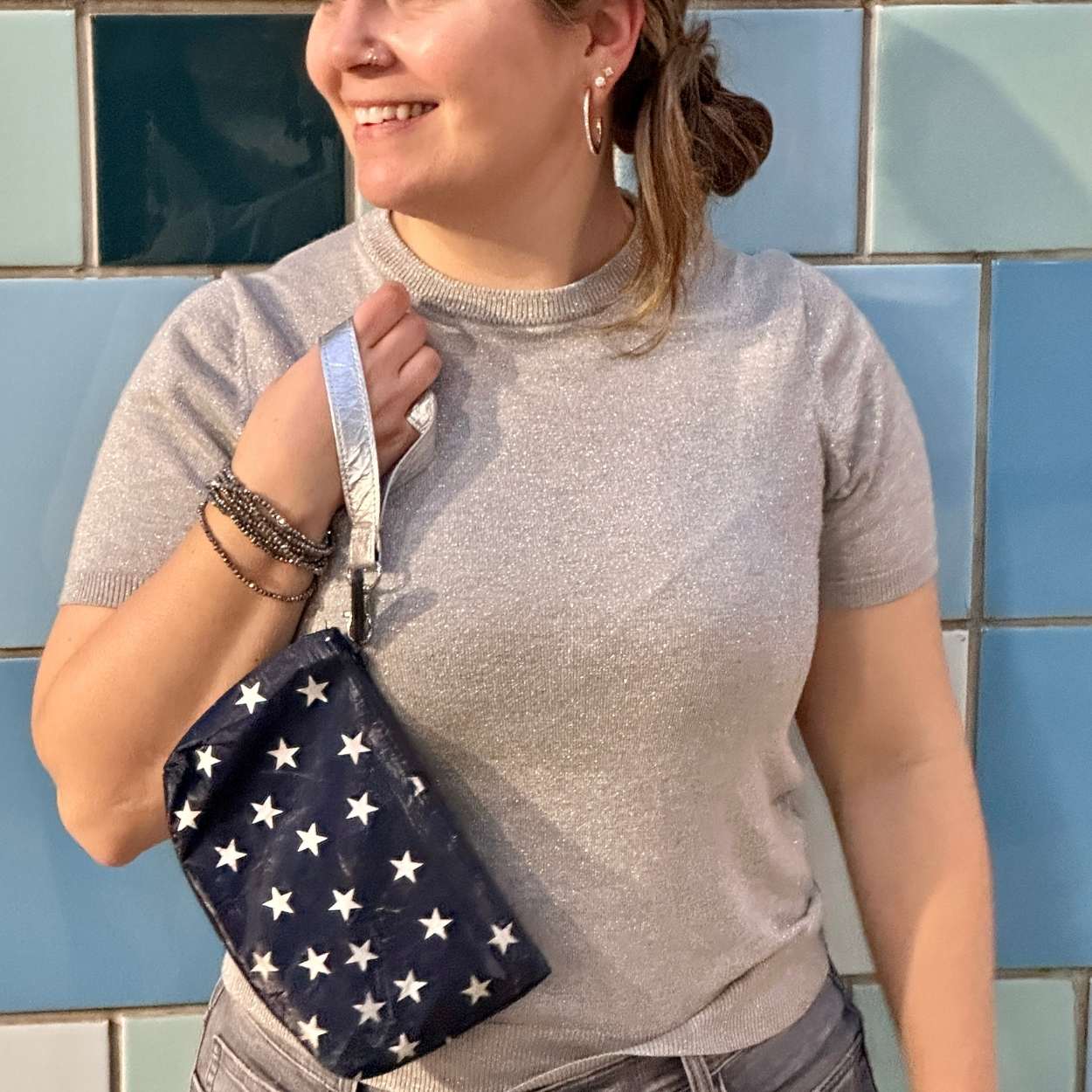 Person holding a navy blue bag with white star patterns against a blue tiled wall.
