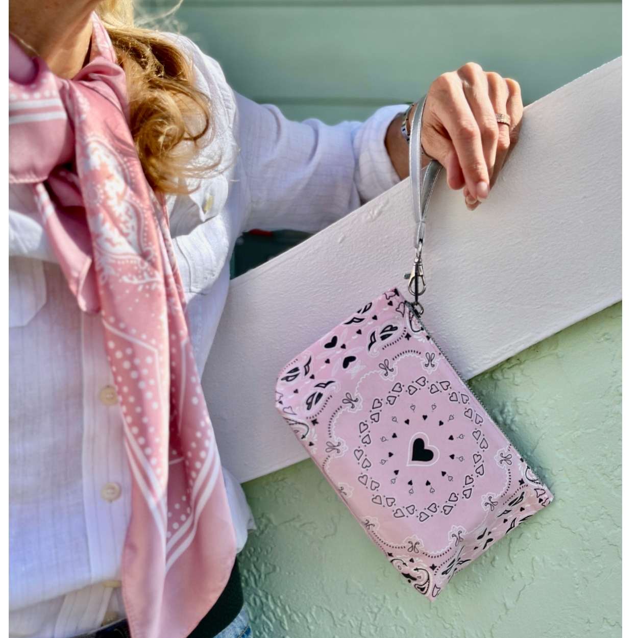 Person holding a pink bandana patterned pouch with a strap against a light green background