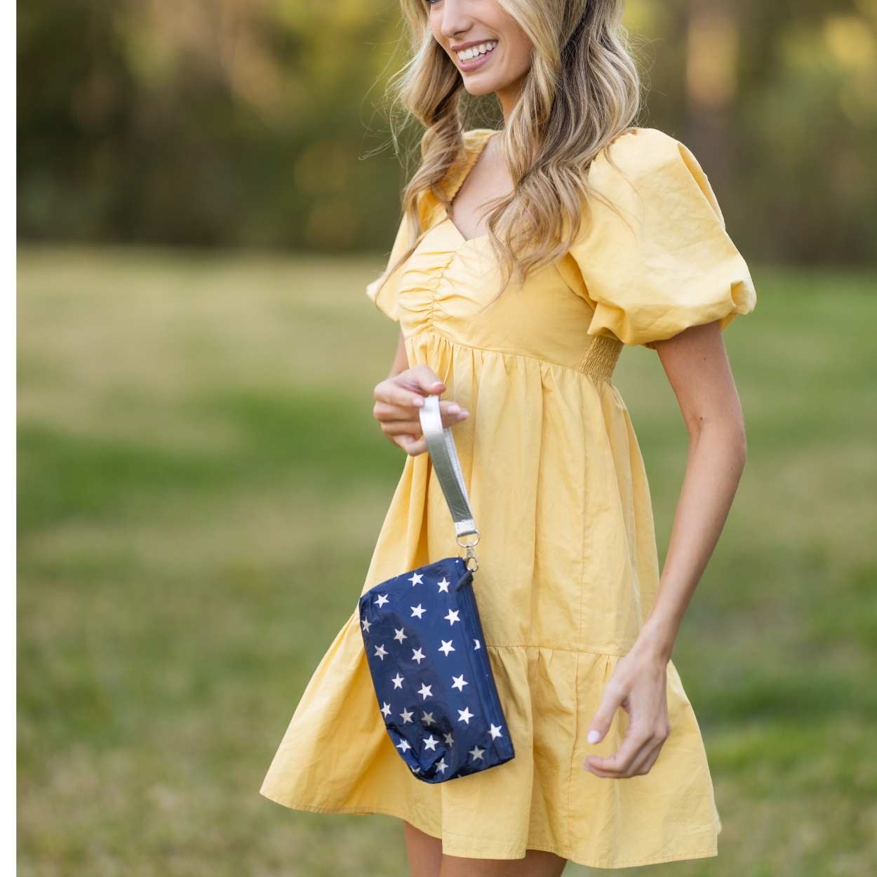 Woman in a yellow dress holding a blue bag with white stars outdoors.
