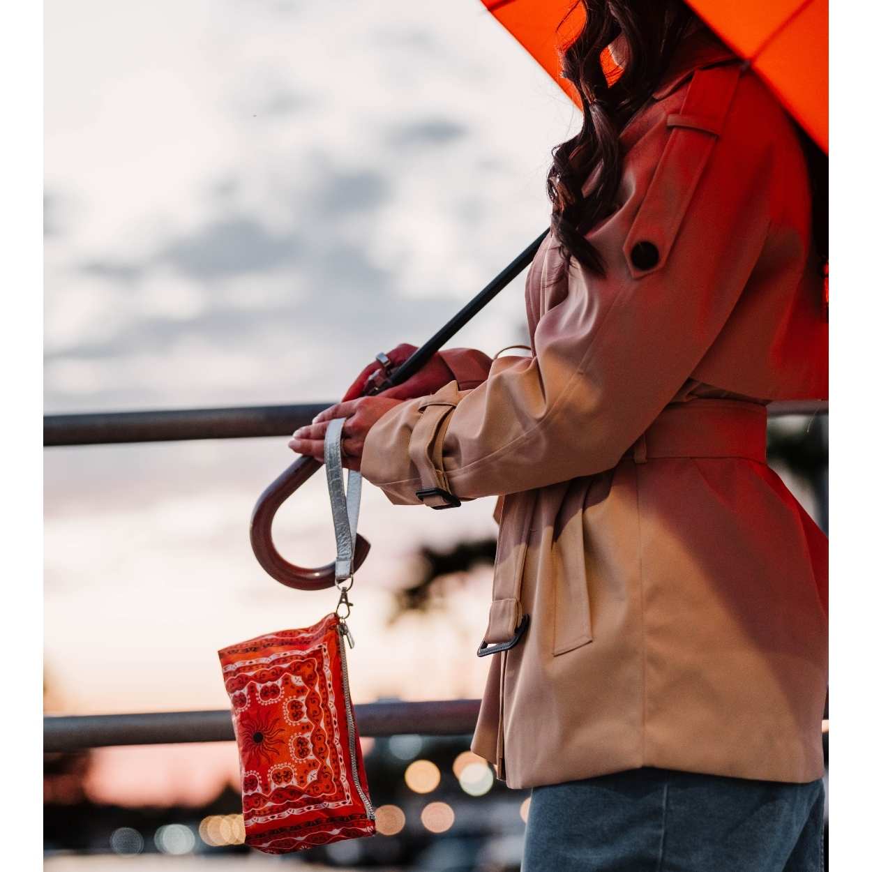 Women with orange umbrella carrying orange bandana print wristlet near canal