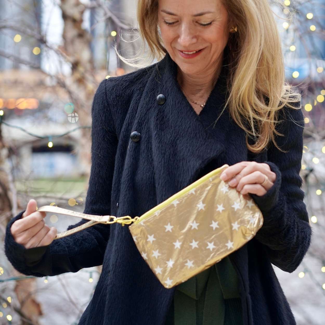 Woman in black jacket outdoors holding zip wristlet in gold with myriad of white stars