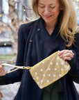 Woman in black jacket outdoors holding zip wristlet in gold with myriad of white stars