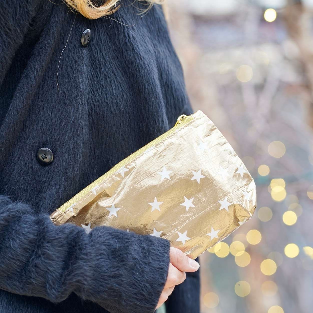 Women in black coat holding zip wristlet in gold with myriad of white stars 