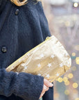 Women in black coat holding zip wristlet in gold with myriad of white stars 