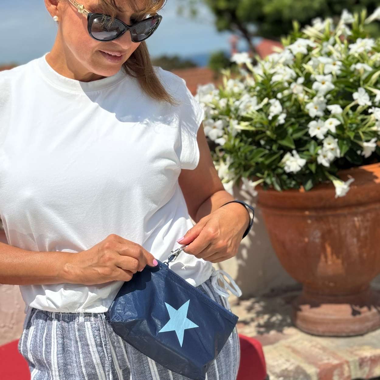Woman outdoors near flowers holding zip wristlet in shimmer navy blue with light blue star
