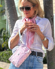 Woman wearing sunglasses, a white shirt, blue jeans, and a pink scarf, holding a matching pink bandana print bag.