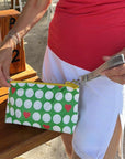 Person holding a green wristlet pouch with white golf balls and red hearts, standing outdoors.