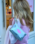 Woman holding a silver wristlet pouch with a pink lip print in front of a store entrance.