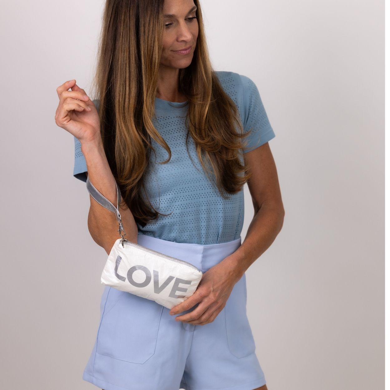 Woman dress in blue holding a wristlet printed with the word LOVE on it.