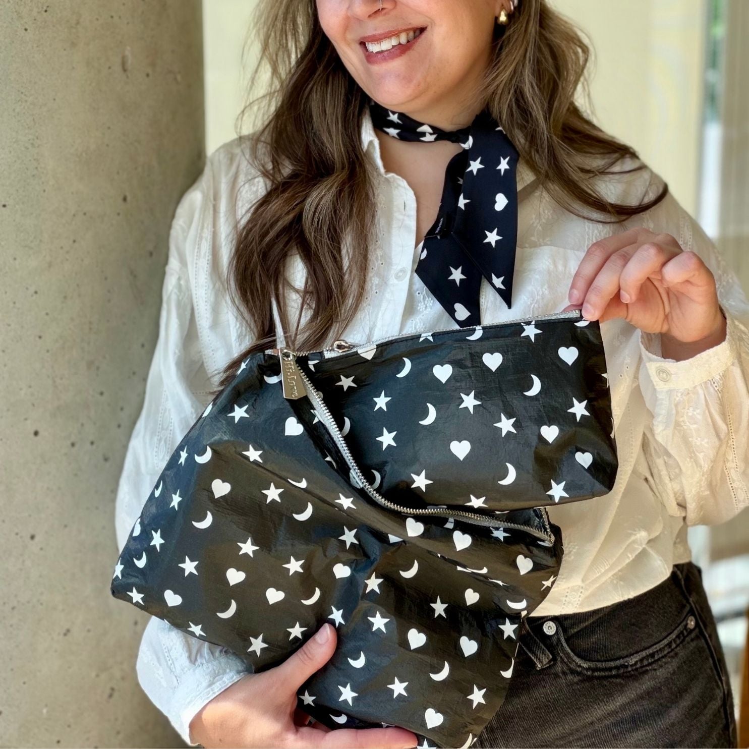 woman holding a set of two zipper pouches that are shimmer black with white heart moon and star on them.
