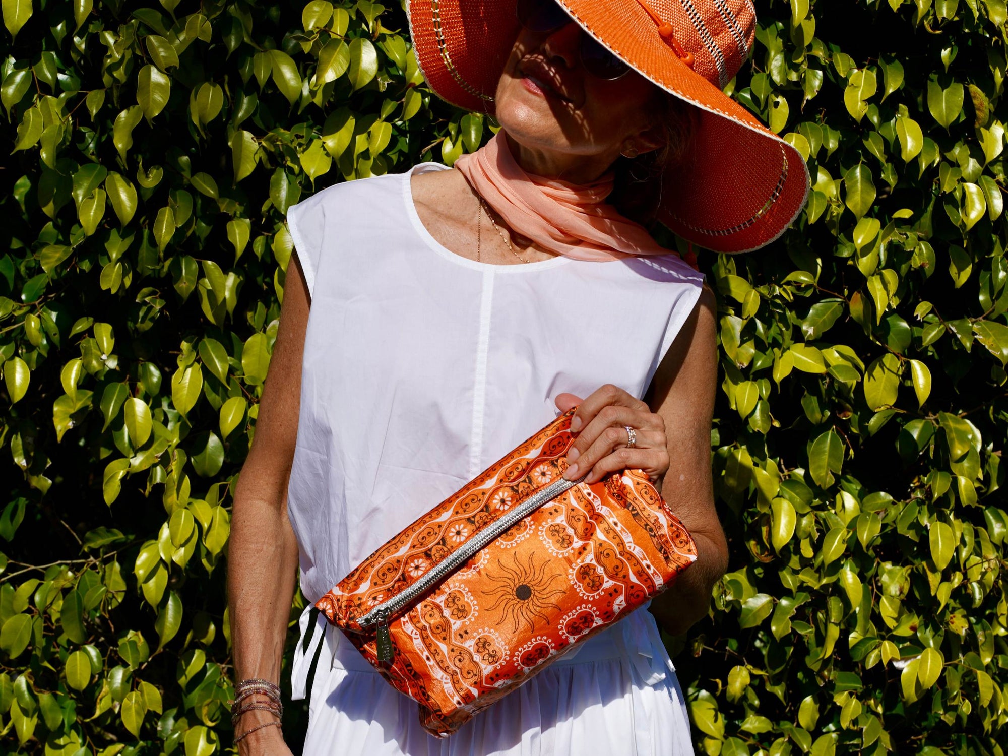 Woman holding an orange bandana pouch  as a clutch against a green leafy background