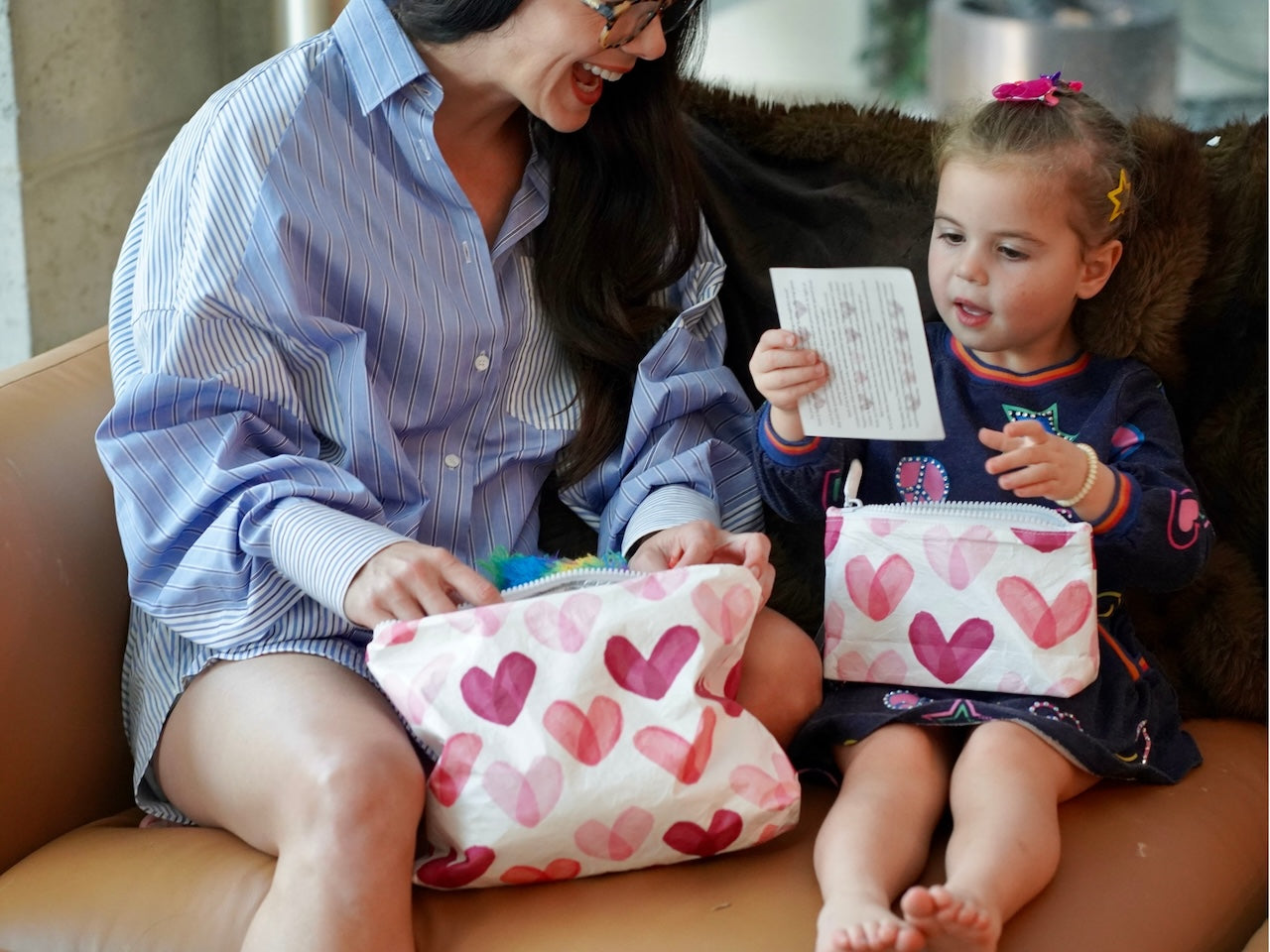 Woman and child sitting on a couch with a set of two heart print zipper pouches
