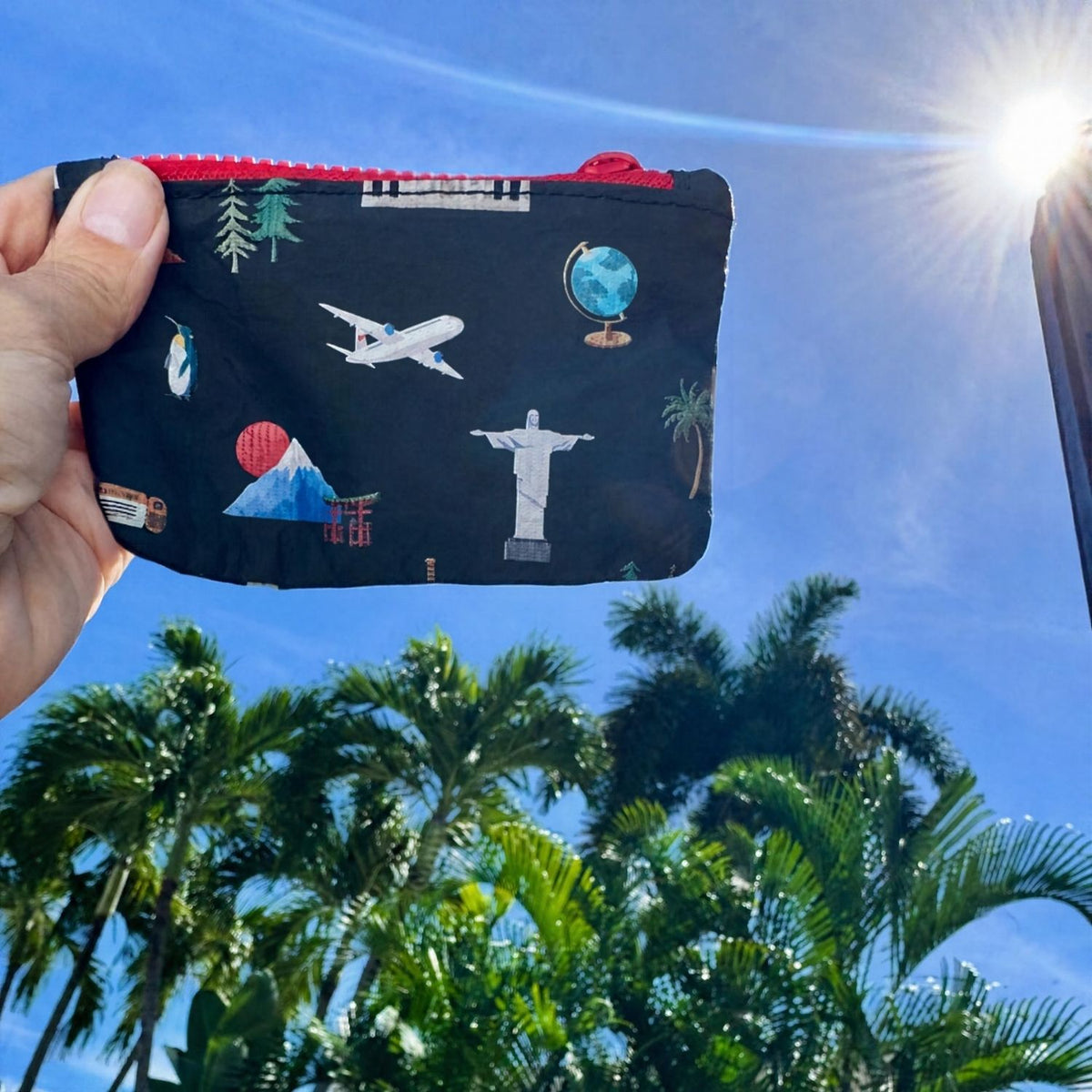 Little zipper wallet with landmarks from the seven continents set against a blue sky and palm trees.