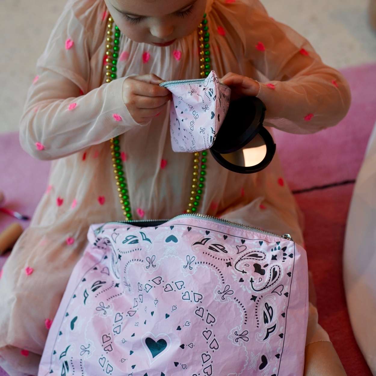 Child holding a pink bandana patterned pouch with a mirror inside