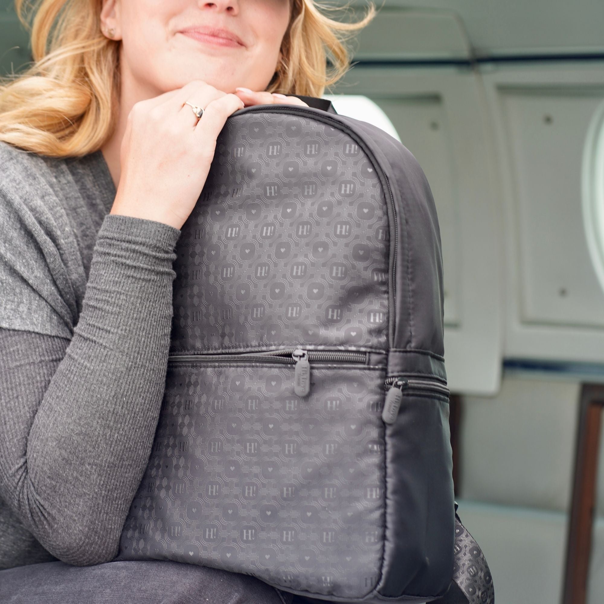 Woman resting her chin on her hand beside the black signature backpack near a plane door.