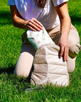 Person pulling pouch with bees on it from beige backpack on grass