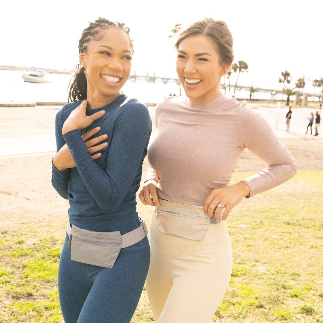 Two women standing outdoors on a sunny day, wearing belt bags.