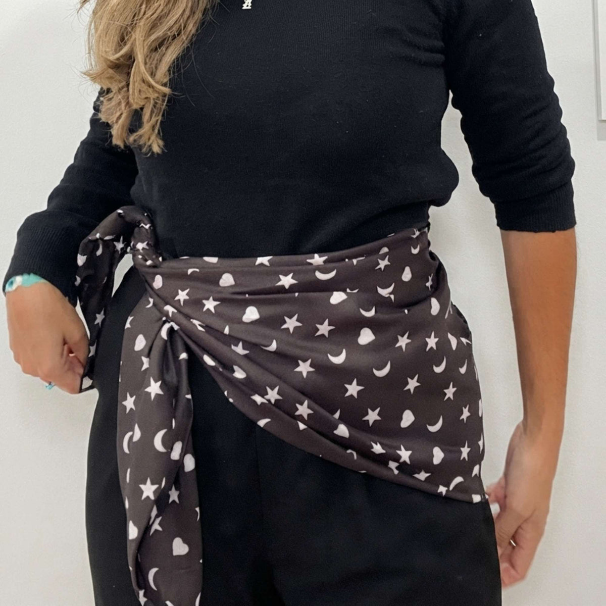 Model wearing the black Signature scarf with white hearts, moons and stars tied around her waist over a black outfit.
