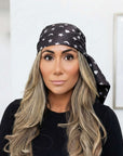 Model wearing a black scarf with white hearts, moons and stars styled as a headscarf, with the ends draped behind her.