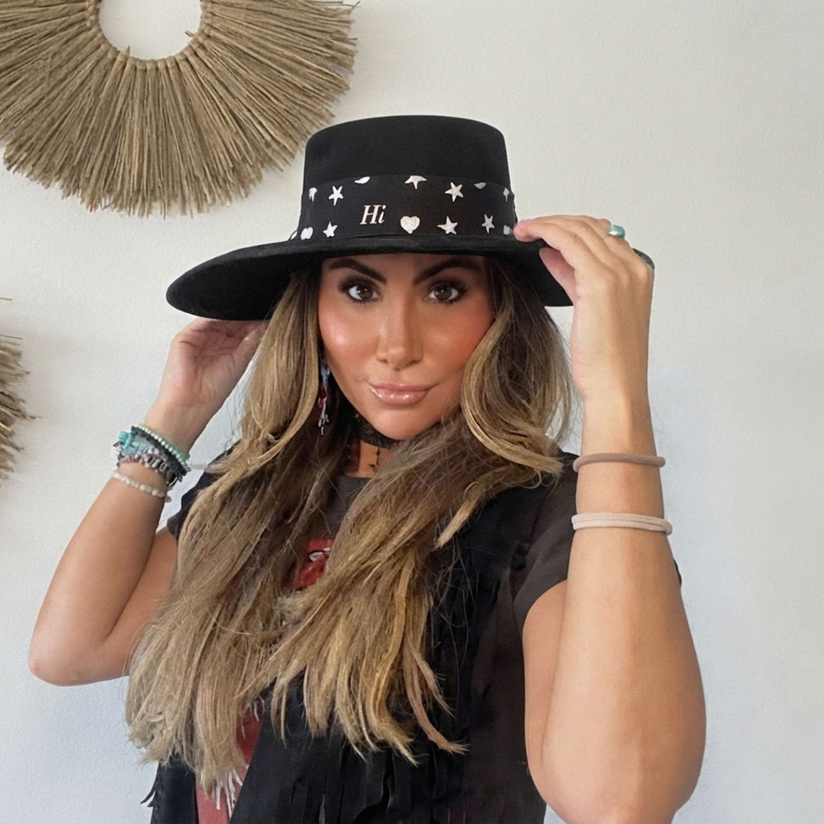 Woman wearing the black Signature scarfette with white hearts, moons and stars wrapped as a hat band around a black western hat.