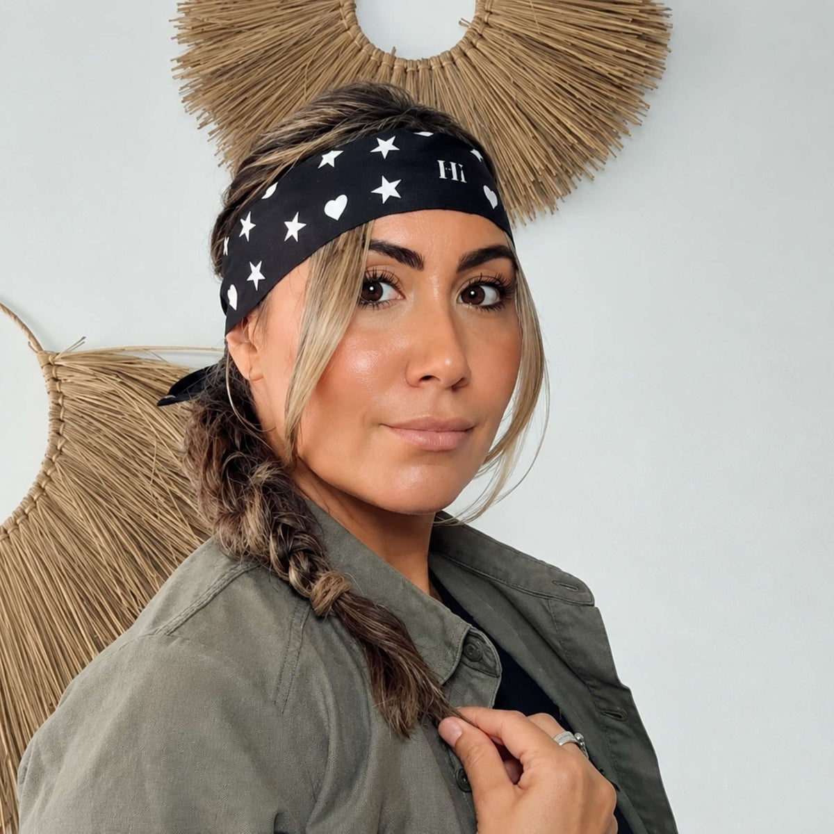 Woman wearing the black Signature scarfette with white hearts, moons and stars as a wide headband with a braid.