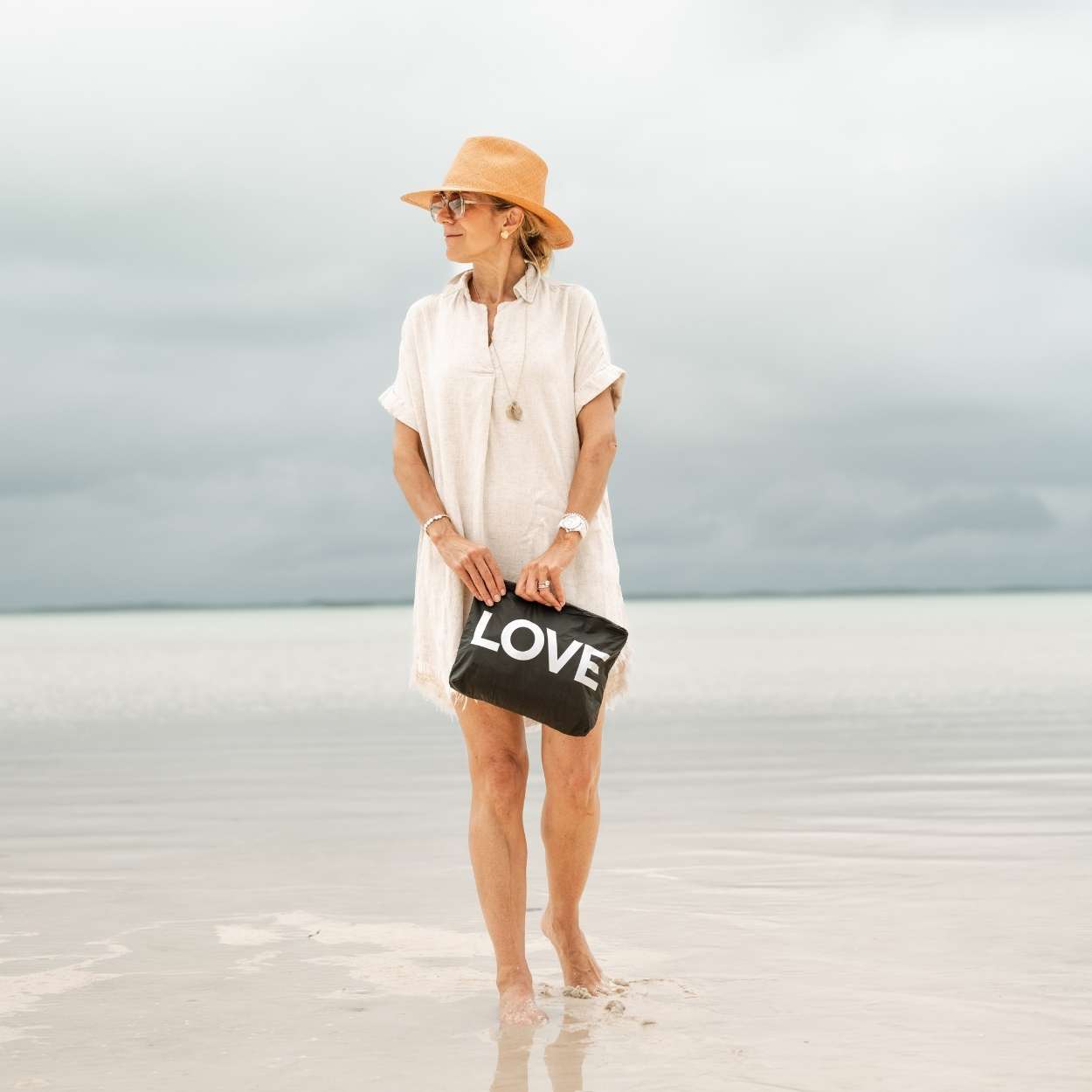 Woman holding a black 'LOVE' pouch on a beach