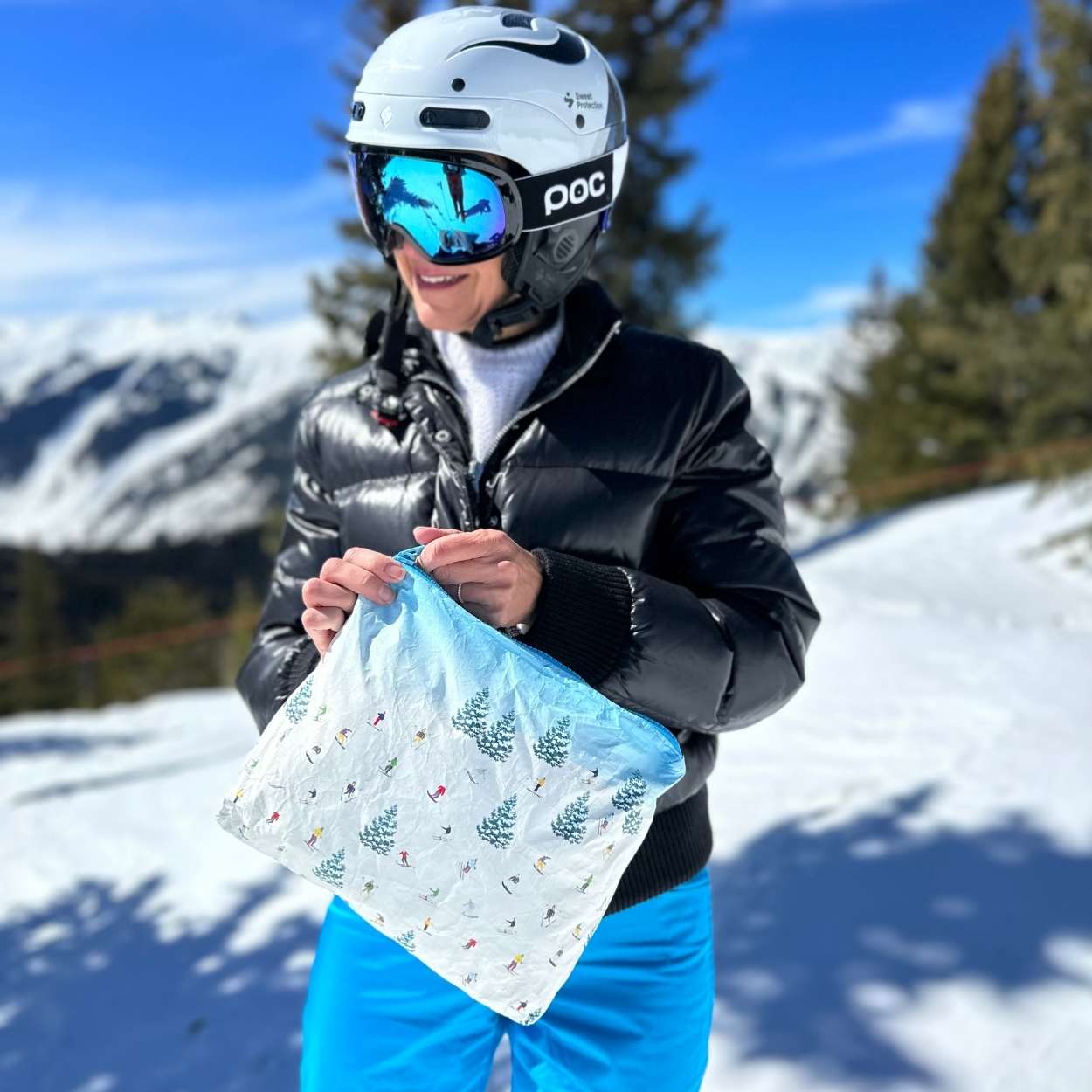 Women in wearing ski helmet and goggles holding the bluebird ski day medium zipper pouch