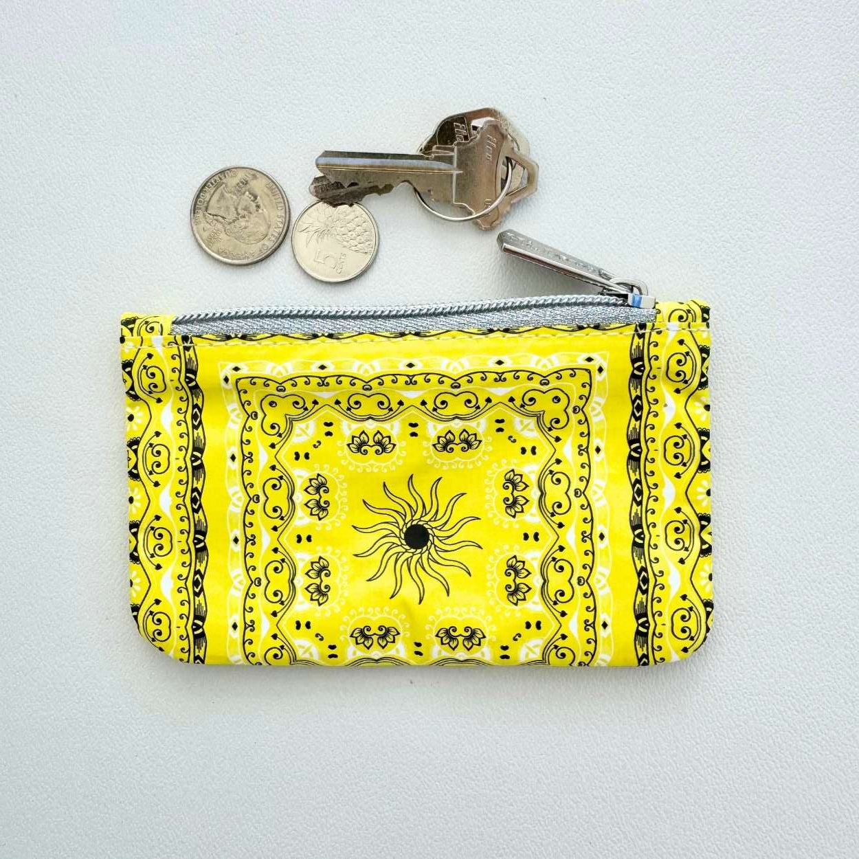 Yellow bandana patterned pouch with keys and coins on a light gray background