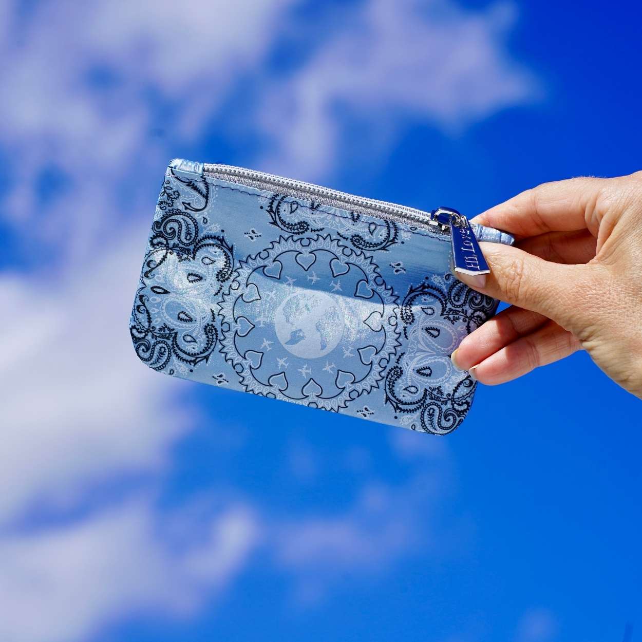 Hand holding a blue bandana patterned pouch against a blue sky background