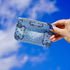 Hand holding a blue bandana patterned pouch against a blue sky background