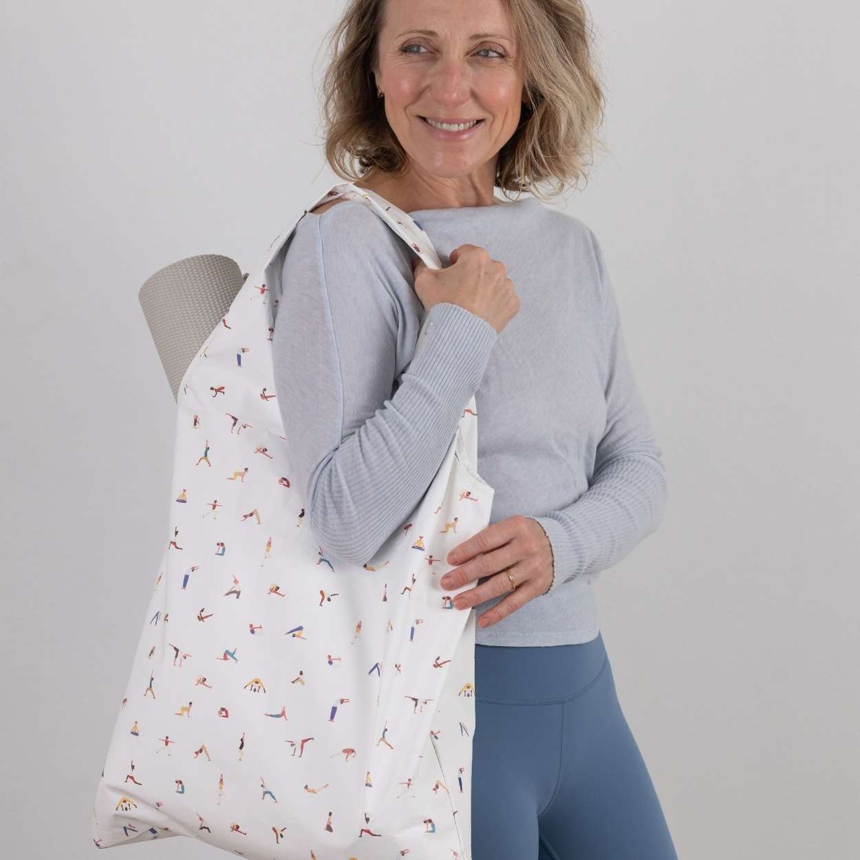 Woman holding a yoga patterned bag against a plain background