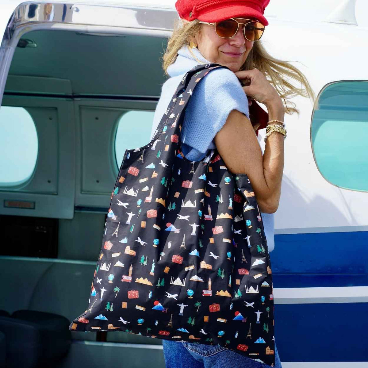 Woman in red hat and sunglasses stepping into plane holding black travel inspired pattern of landmarks from the seven continents. 