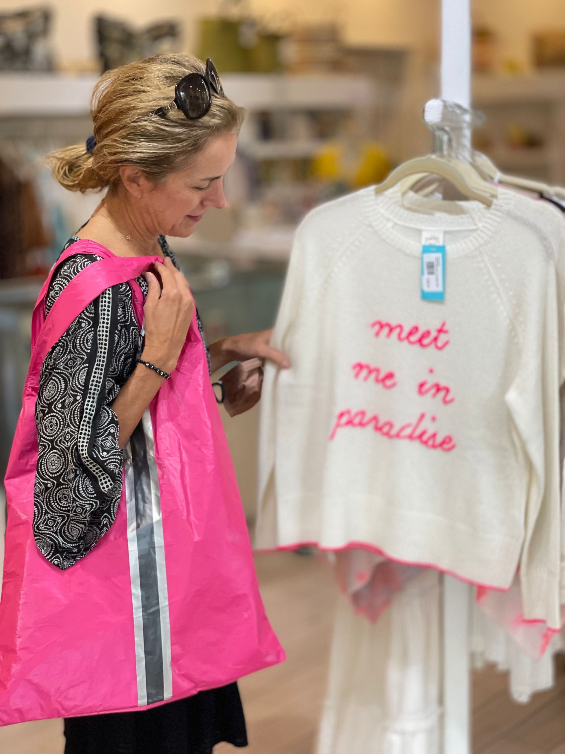 Woman shopping in Harbour Island carrying carryall tote bag in pink looking at cream sweater 