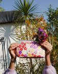 Person holding a floral pouch with flowers against a garden background