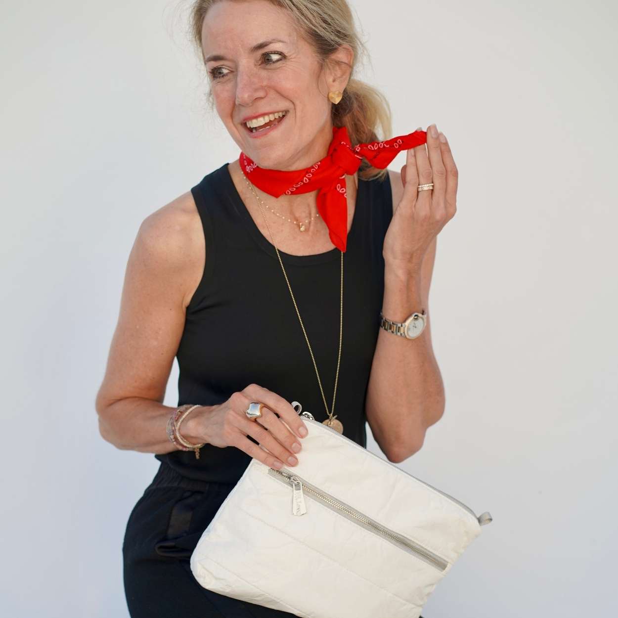 Woman holding a white handbag with a red scarf around her neck against a plain background
