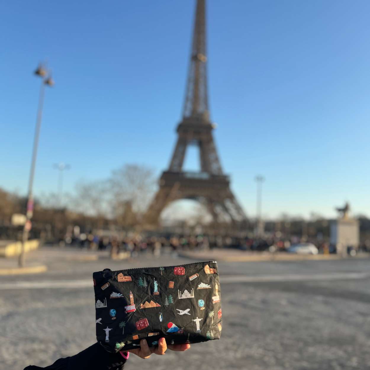 Hand holding a travel patterned pouch in front of the Eiffel Tower